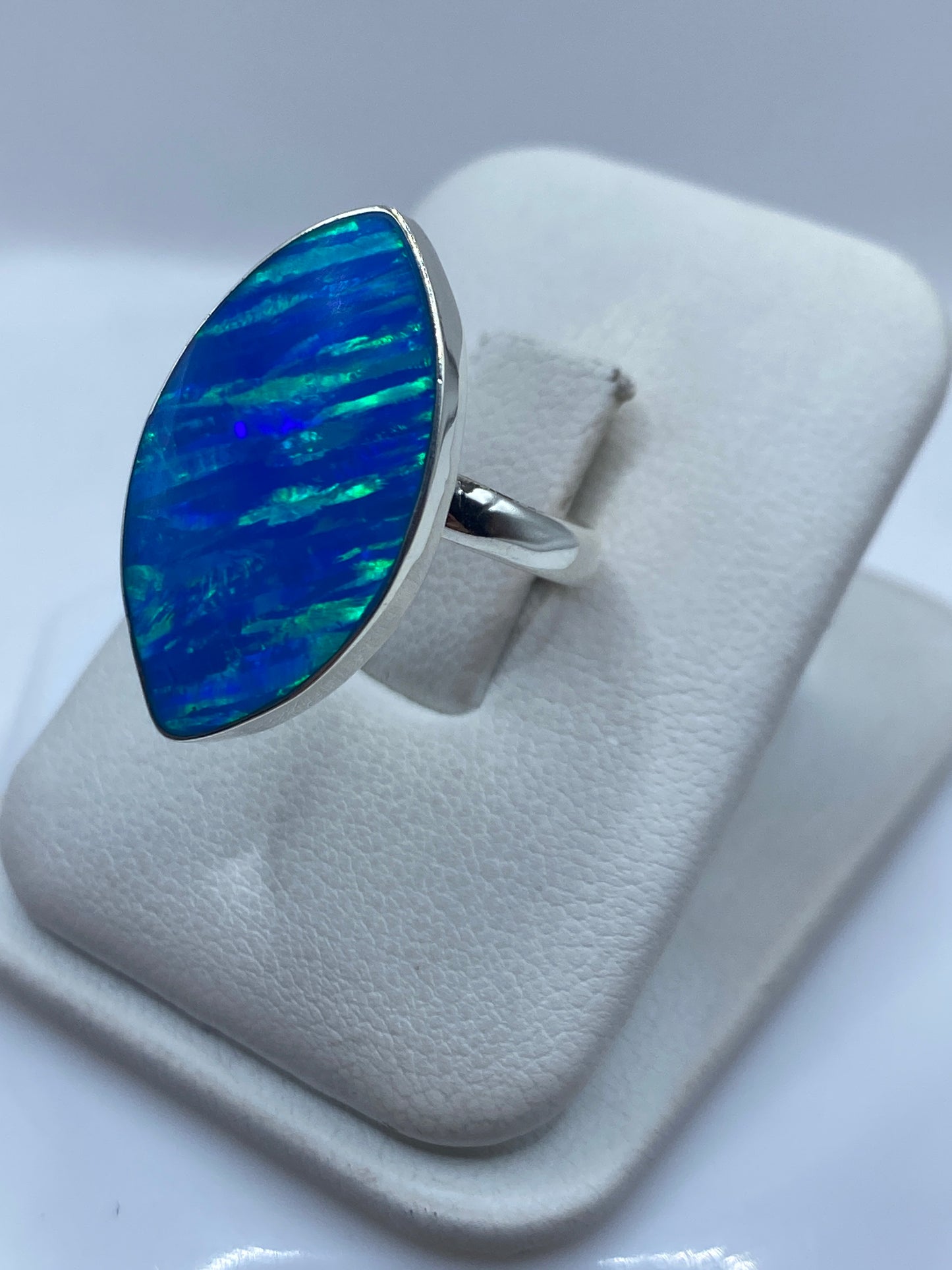 Anillo ópalo de fuego azul en dedo de mujer, mostrando juego de colores verde y azul
