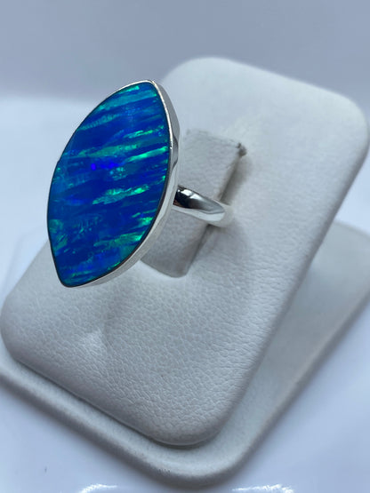 Anillo ópalo de fuego azul en dedo de mujer, mostrando juego de colores verde y azul