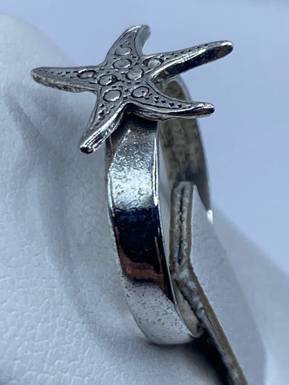 Anillo de plata estrella marina puesto en la mano con textura marina visible