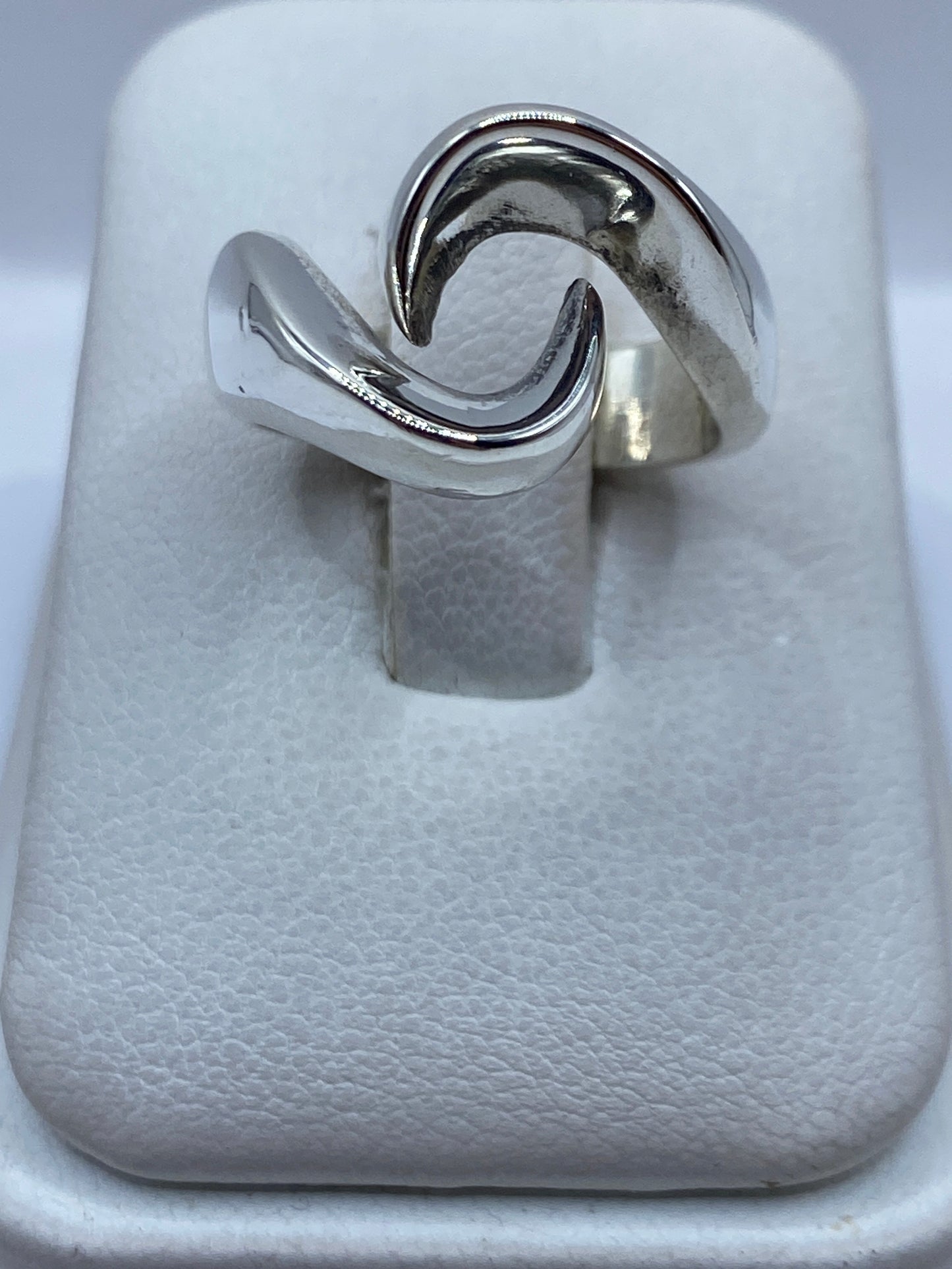 Anillo de plata onda minimalista en la mano de una mujer, mostrando el diseño fluido