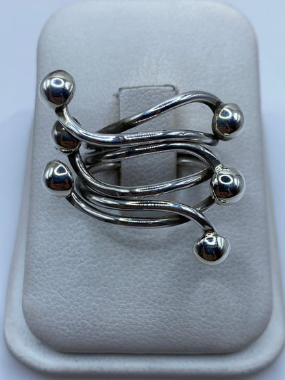Anillo ajustable de plata con tres bandas fluidas y esferas en movimiento, vista frontal en estuche