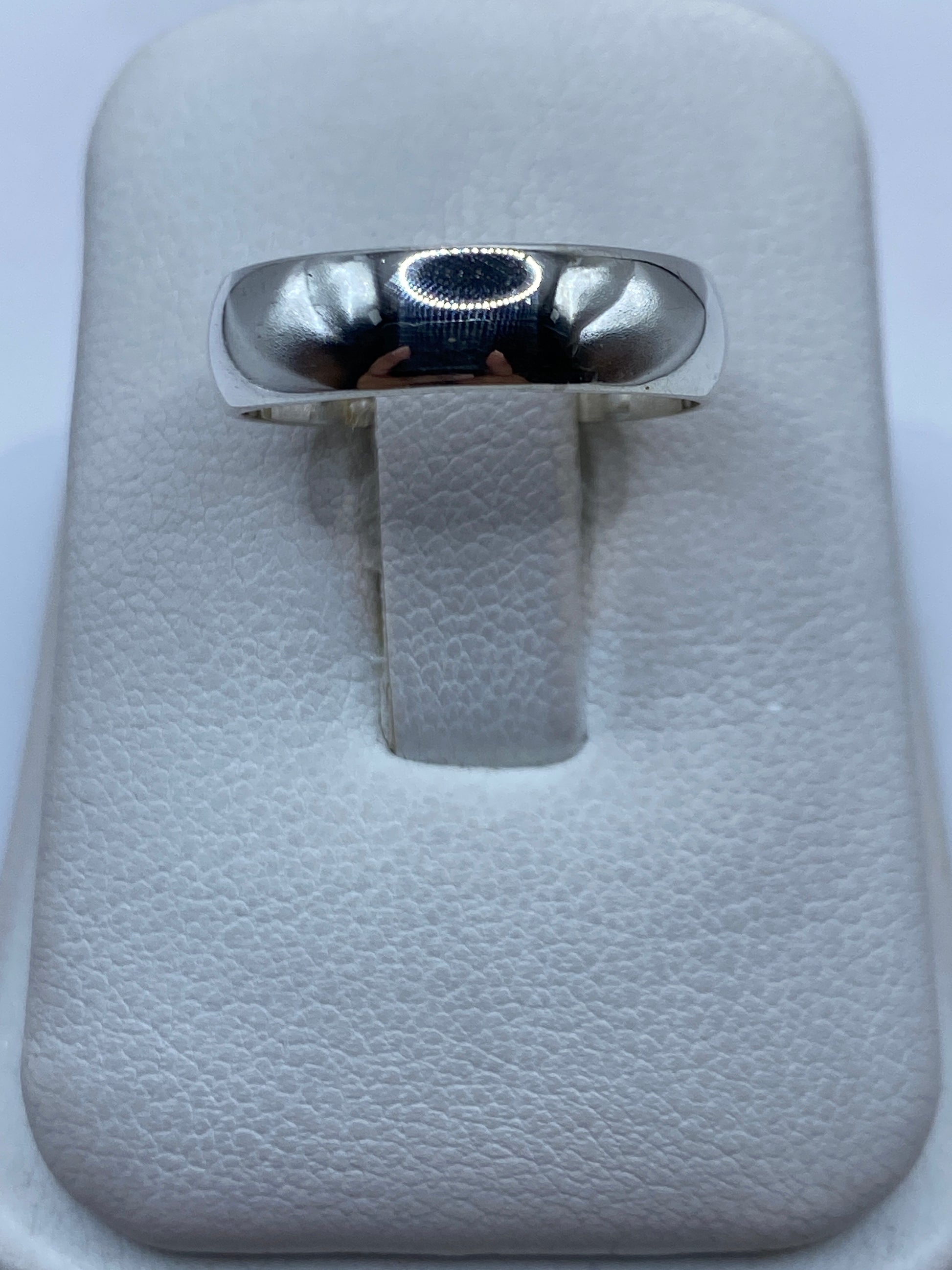 Anillo de plata lisa pulida en una mano, vista frontal de la banda minimalista