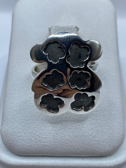 Anillo floral de plata .925 ajustable en vitrina blanca, vista superior de seis pétalos