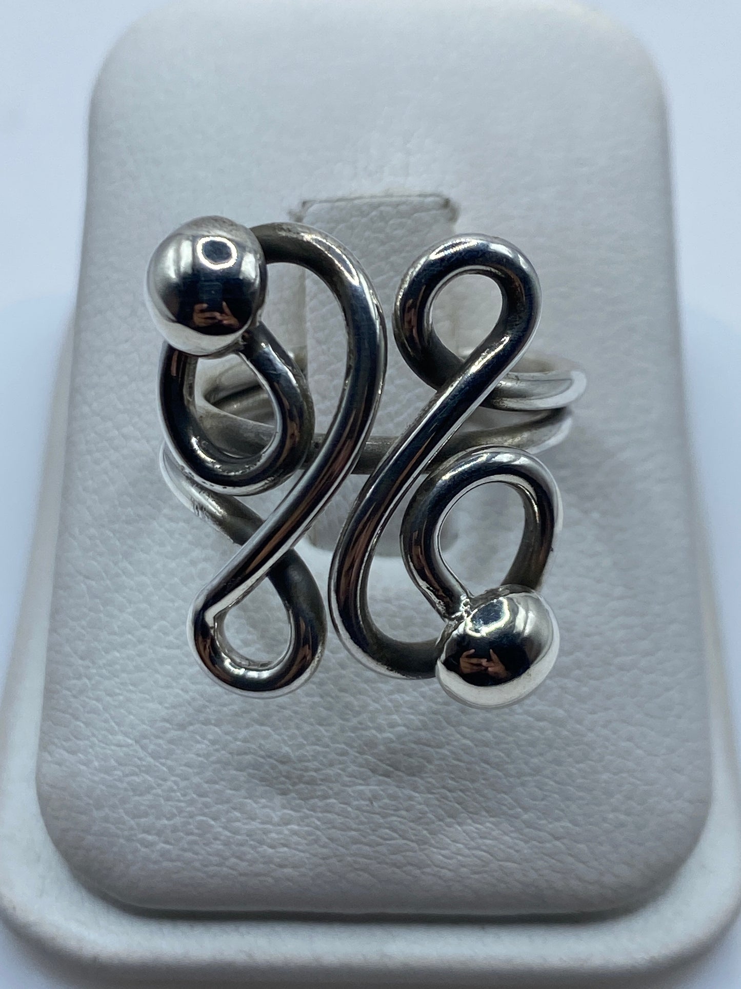 Anillo de plata calado con esferas en bucles geométricos en la mano de una mujer