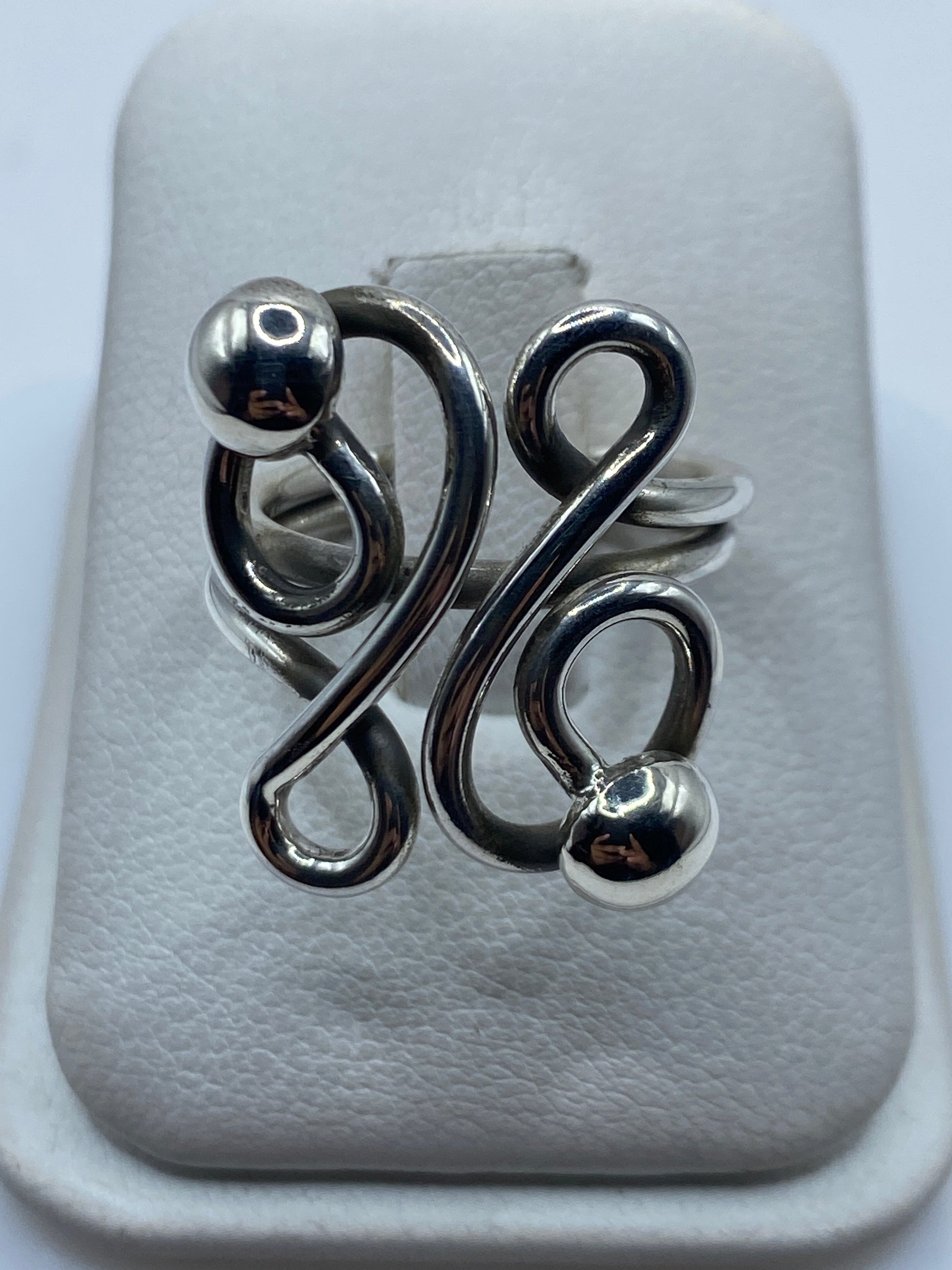 Anillo de plata calado con esferas en bucles geométricos en la mano de una mujer
