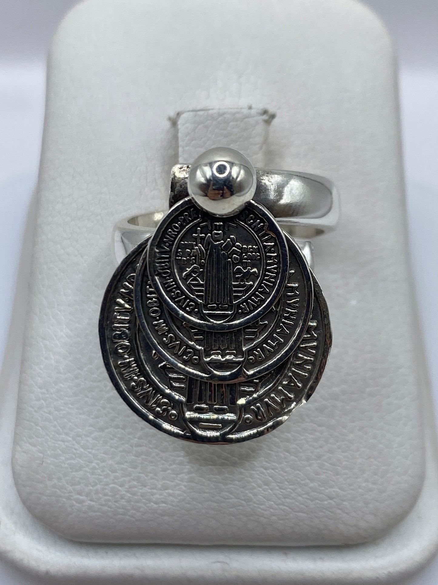Anillo religioso de plata .925 ajustable sobre estuche blanco, visto de frente con detalle de diseño sagrado