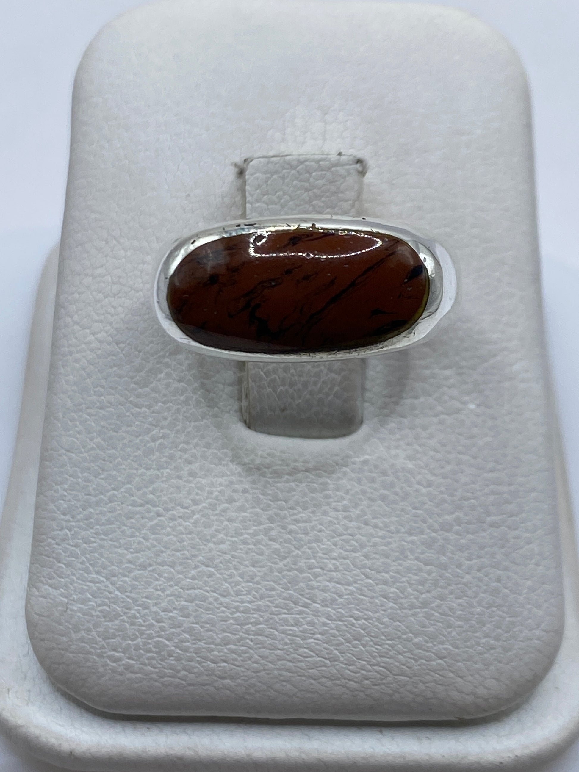 Anillo de plata con piedra café en mano, mostrando el engaste pulido
