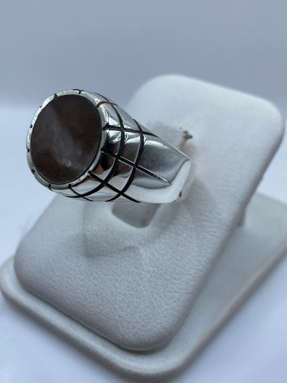 Anillo de plata unisex con engaste a mano de piedra café, de costado en mano