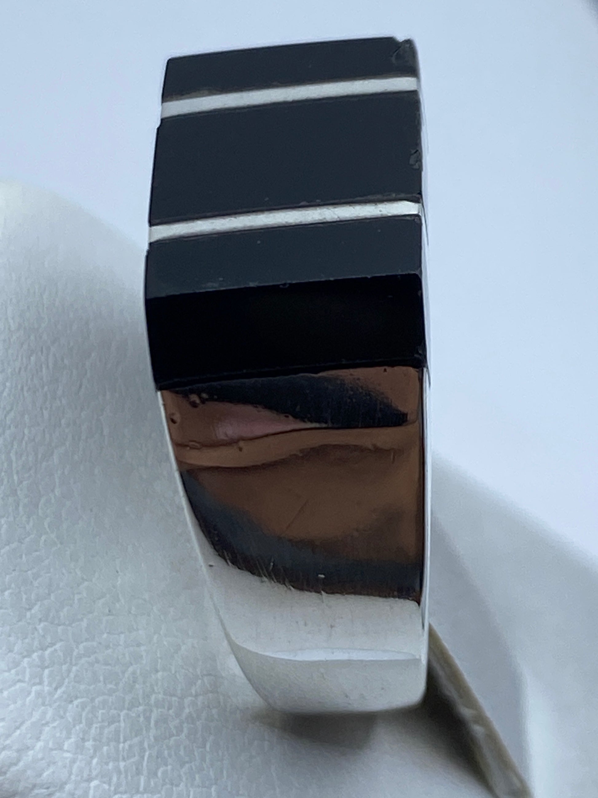 Anillo puesto en dedo de hombre, ónix negro brillante con bandas de plata entre piedras