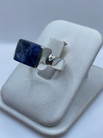 Vista lateral del anillo de coctel con piedra azul en mano de mujer