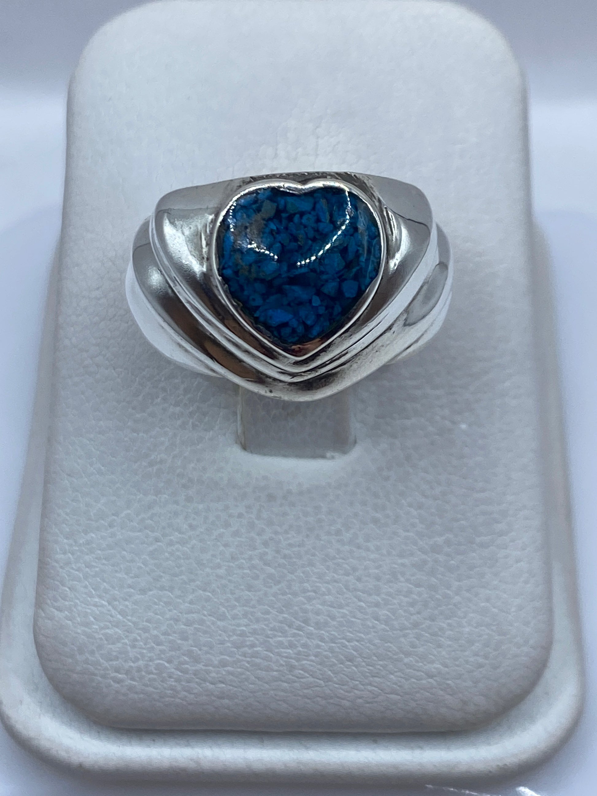 Anillo de plata con forma de corazón y piedra azul sobre fondo blanco