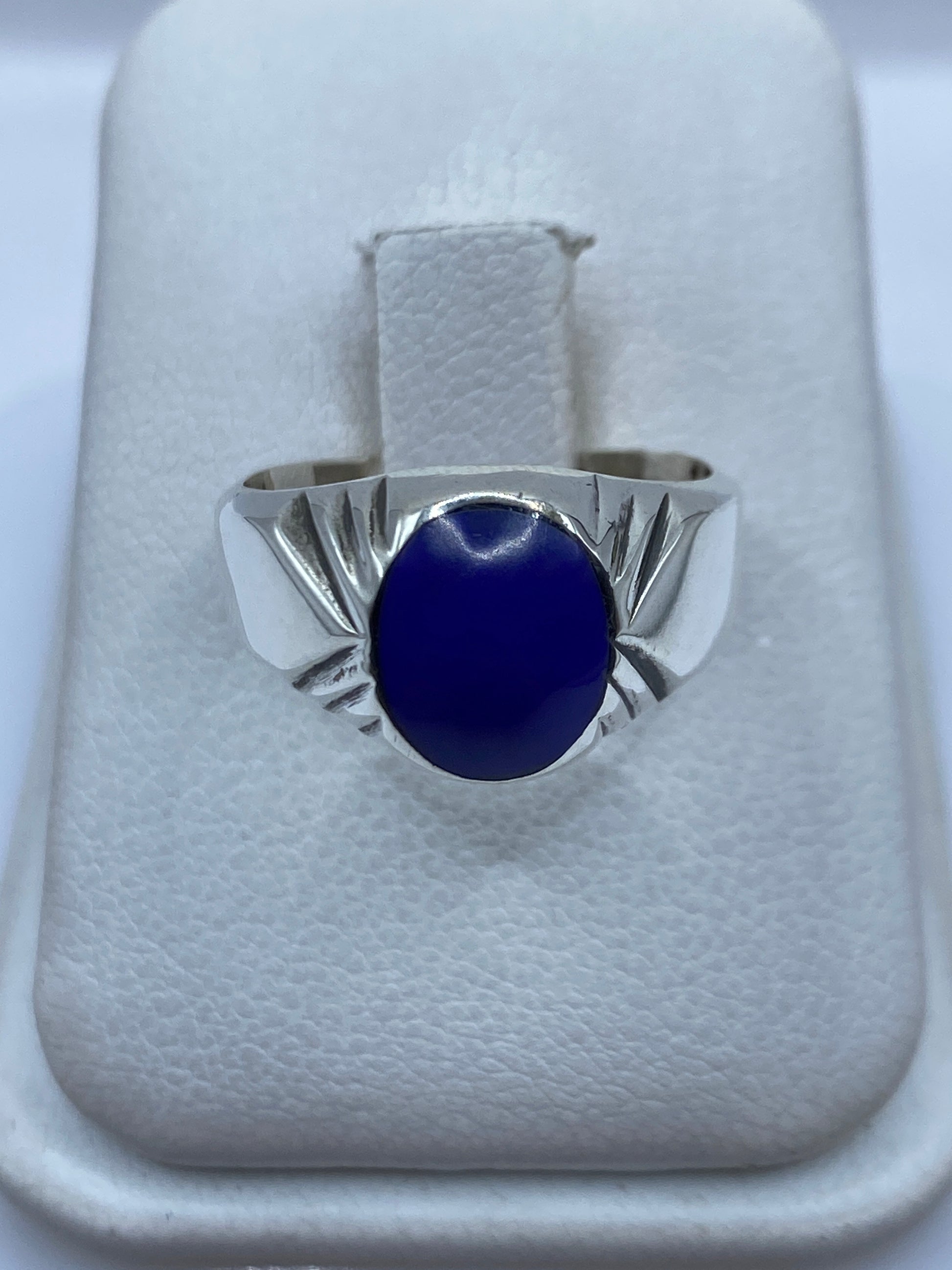 Anillo de plata con piedra azul engastada, visto de frente sobre dedo con manicura neutra