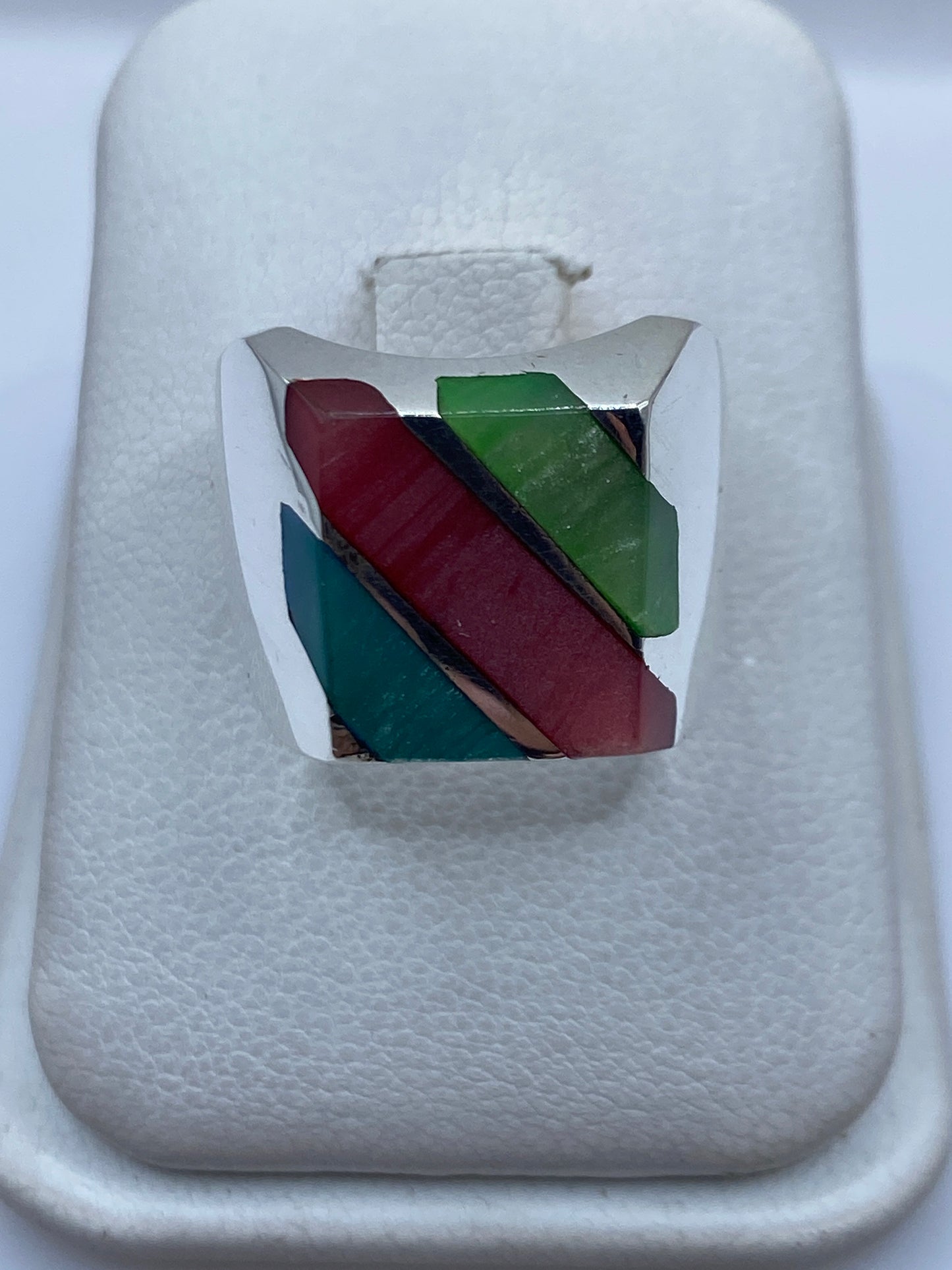 Anillo de plata con incrustación multicolor de piedras rojo, verde y azul teal sobre fondo blanco