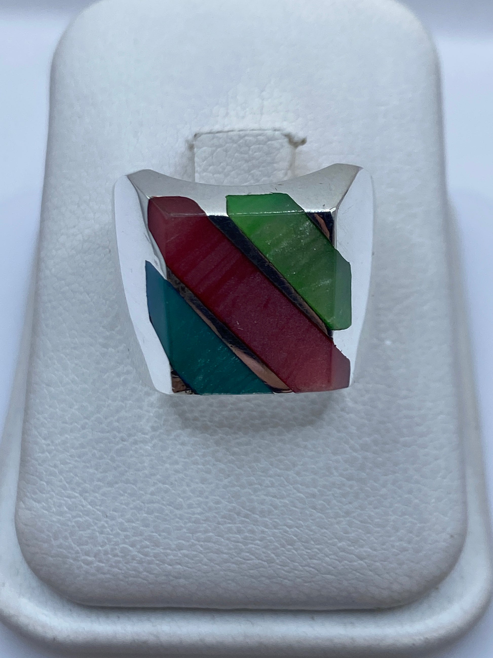 Anillo de plata con incrustación multicolor de piedras rojo, verde y azul teal sobre fondo blanco