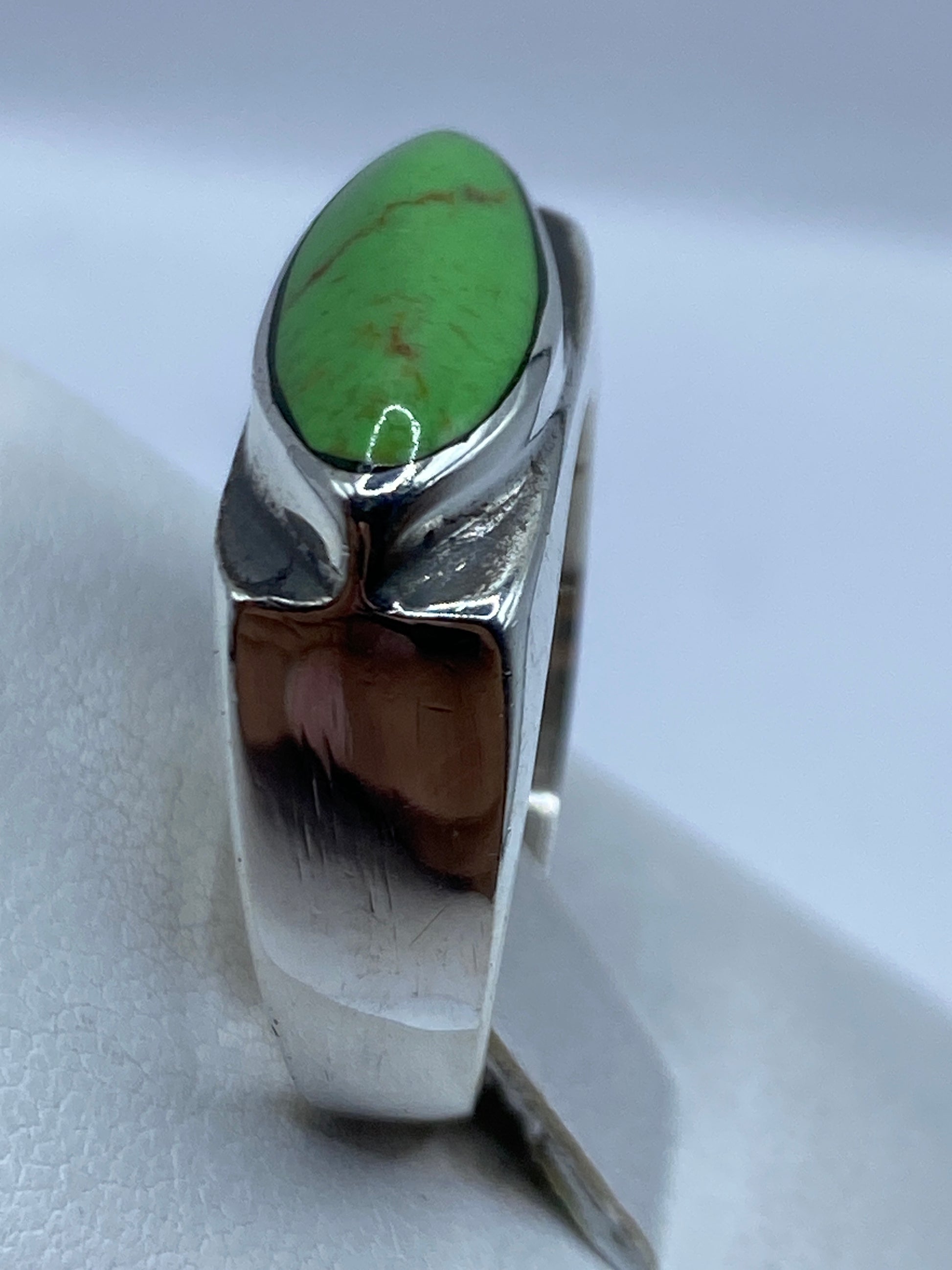 Anillo en dedo, piedra verde brillando contra la piel, diseño limpio y geométrico