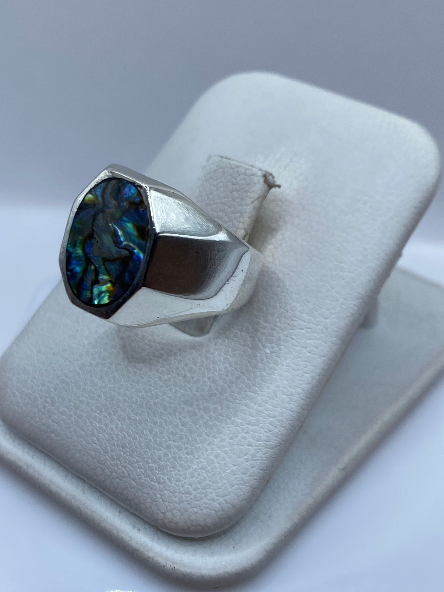 Anillo de plata en la mano, mostrando el engaste delicado de la piedra con brillo azul y verde