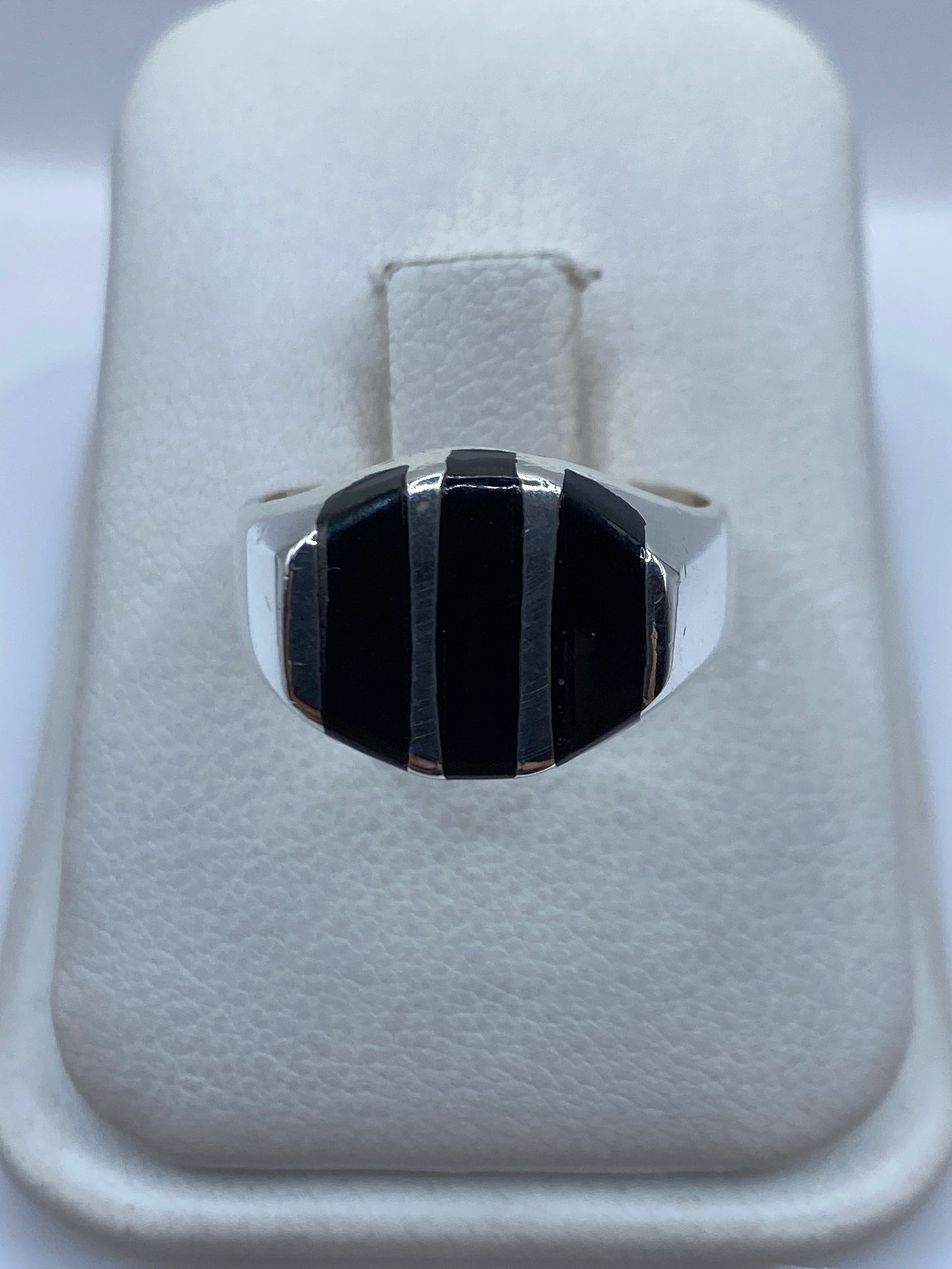 Anillo de plata con ónix negro en franjas escalonadas, vista frontal sobre estuche blanco