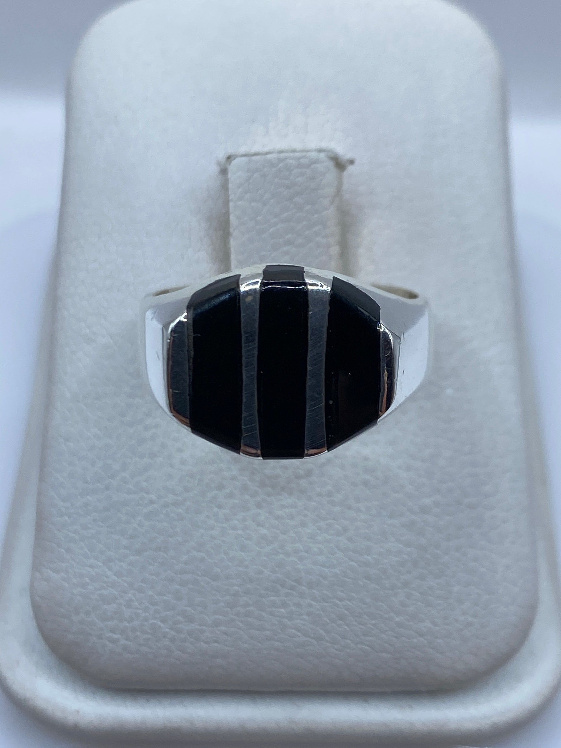 Anillo de plata con ónix negro en franjas escalonadas, vista frontal sobre estuche blanco