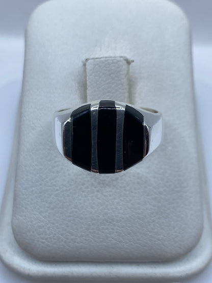 Anillo de plata con ónix negro en franjas escalonadas, vista frontal sobre estuche blanco